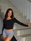 Woman in black long-sleeve top and gray shorts standing on a staircase.